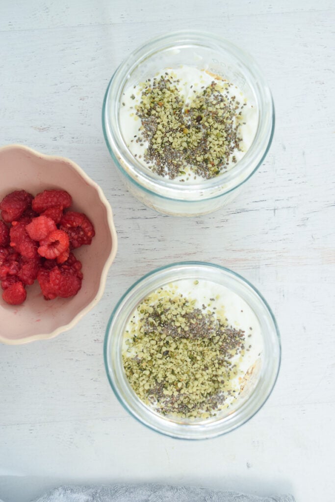 layered mason jars for overnight raspberry oats with bowl of raspberries nearby to add on top