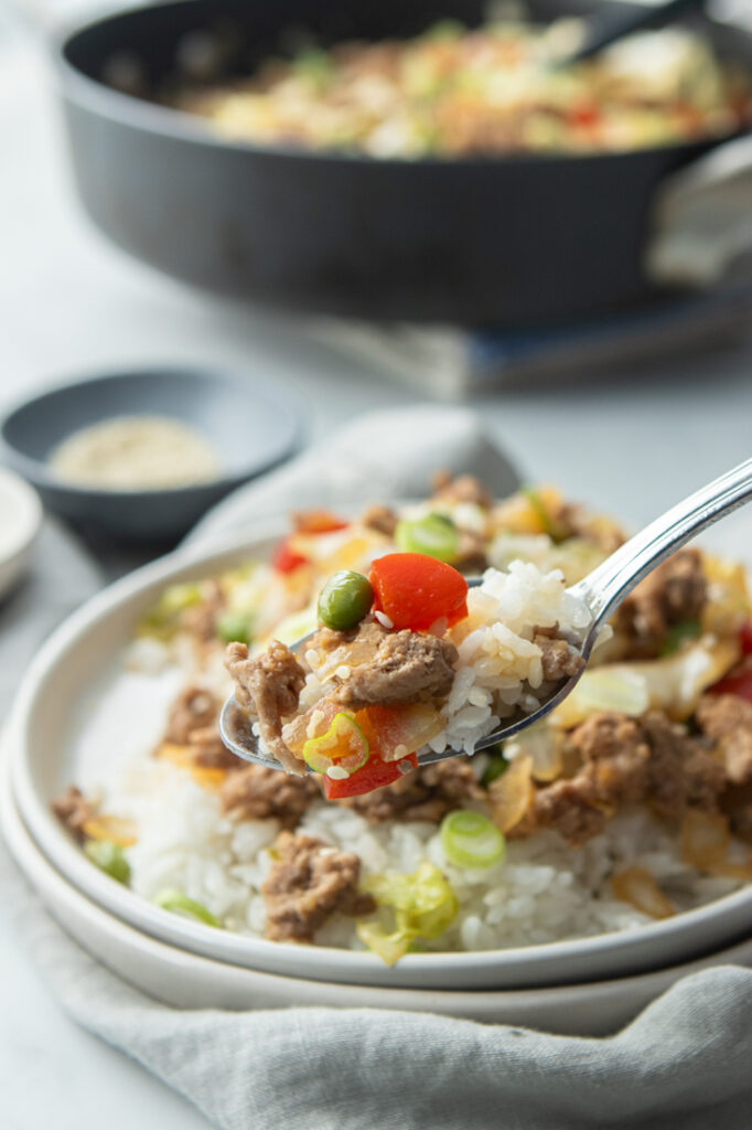 forkful of pork and veggie stir fry on white plate served with white rice