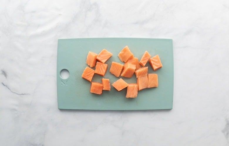 small salmon bite squares on teal cutting board