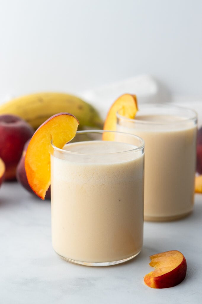 banana peach smoothie in two glasses with peaches on rims