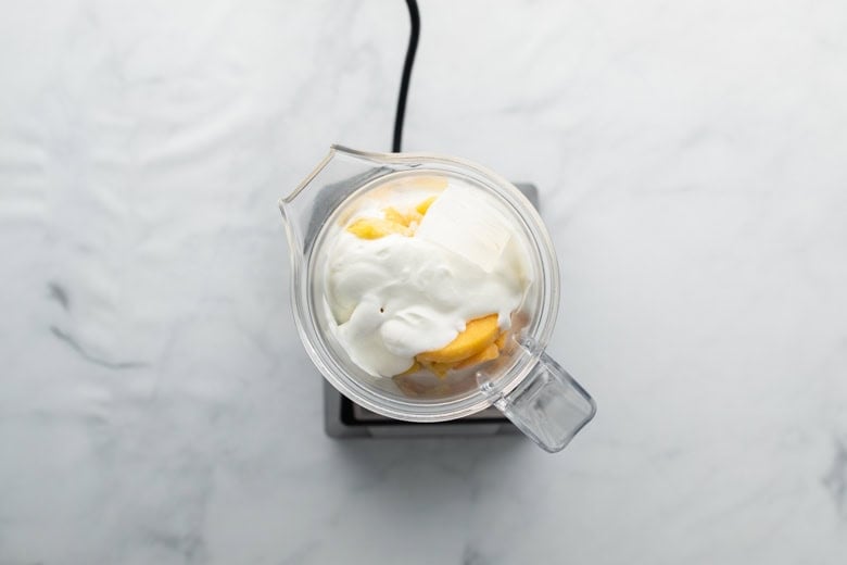 Blender with ingredients to make a creamy smoothie with peach and banana and greek yogurt