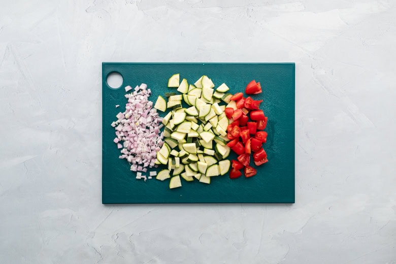 teal cutting board with diced shallot, zucchini and tomato