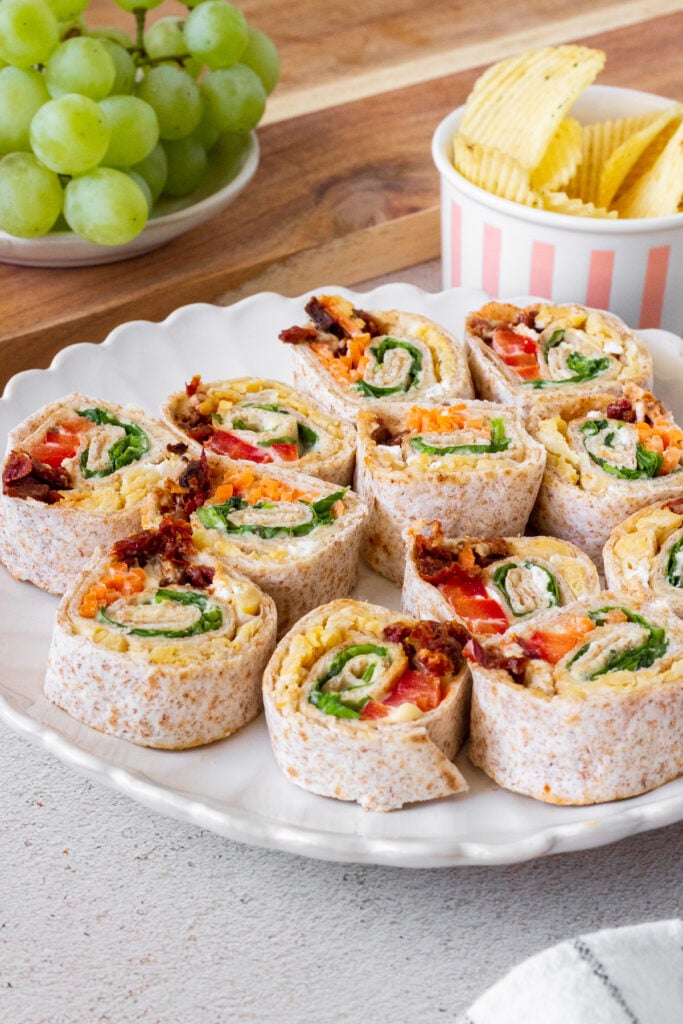 rolled up hummus veggie pinwheels on white plate with spinach, tomatoes, and carrots inside. 