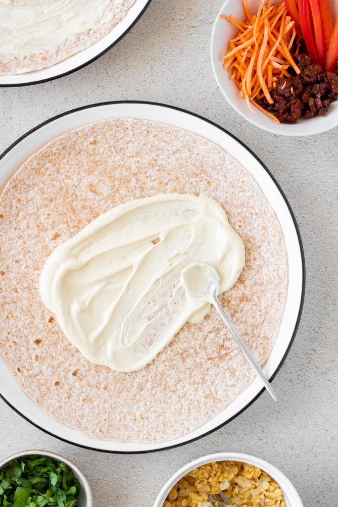 spreading hummus on tortilla for hummus pinwheels