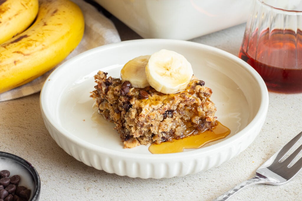 white bowl with banana oatmeal chocolate chip bar, topped with syrup and banana