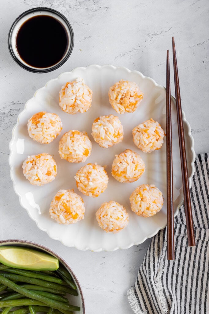 Circular salmon rice balls on a white plate with soy sauce and chopsticks.