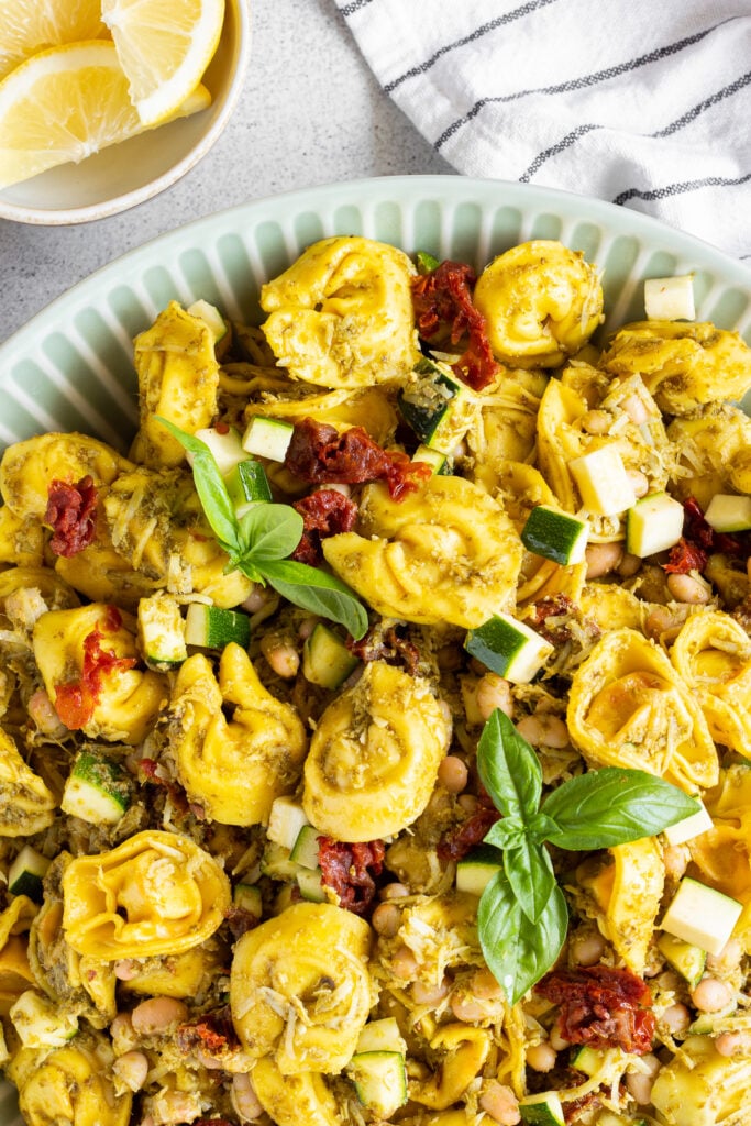 close up of tortellini pesto pasta salad, garnished with basil and sundried tomatoes.