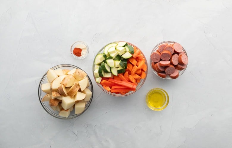 chopped potatoes, zucchini, carrots, peppers and kielbasa in clear bowls