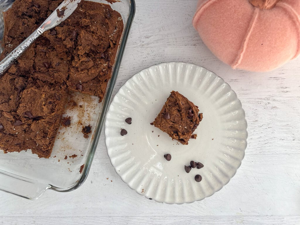 Pumpkin chocolate brownie on white plate next to 8x11 baking dish of brownies.